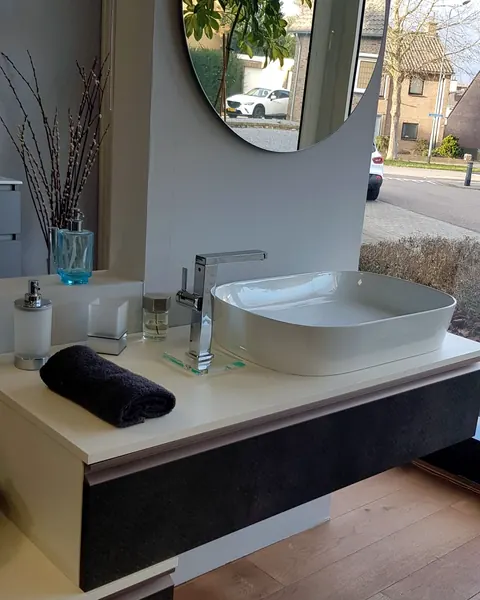 Wastafelmeubel met ronde spiegel en opzetwastafel bij het raam in de showroom van Jos Nelissen in Stein